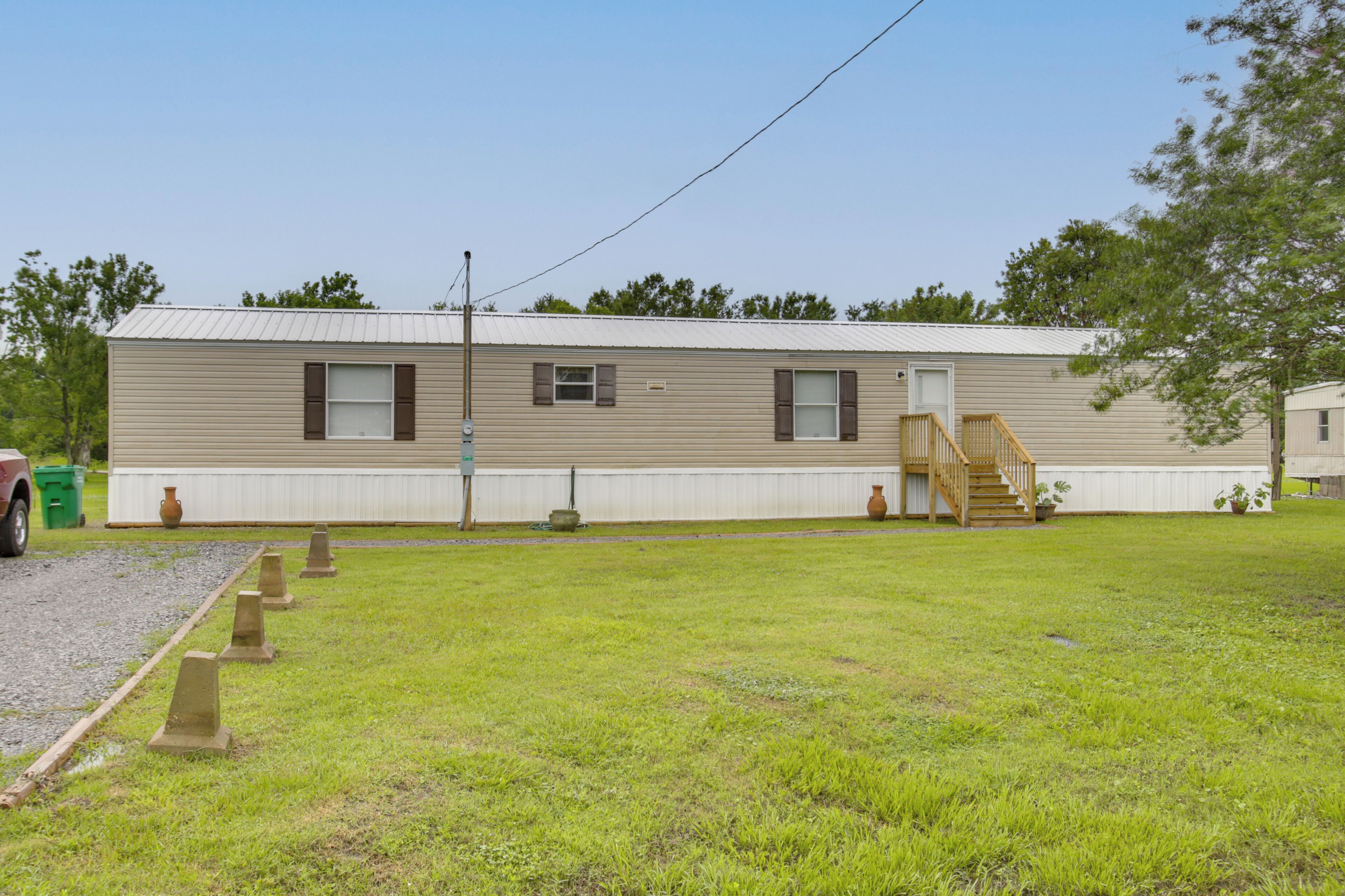 A single-story mobile home with a front porch, a staircase, and a small yard.