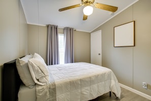 A bedroom with a bed, a ceiling fan, a window with curtains, and a door.