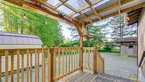 A wooden deck with a metal roof, a gravel path, and a small shed in the background. - Pet-friendly Quaint Cottage: Park-like Setting (Monroe)