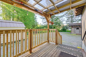 A wooden deck with a metal roof, surrounded by trees and a gravel path. - Pet-friendly Quaint Cottage: Park-like Setting (Monroe)