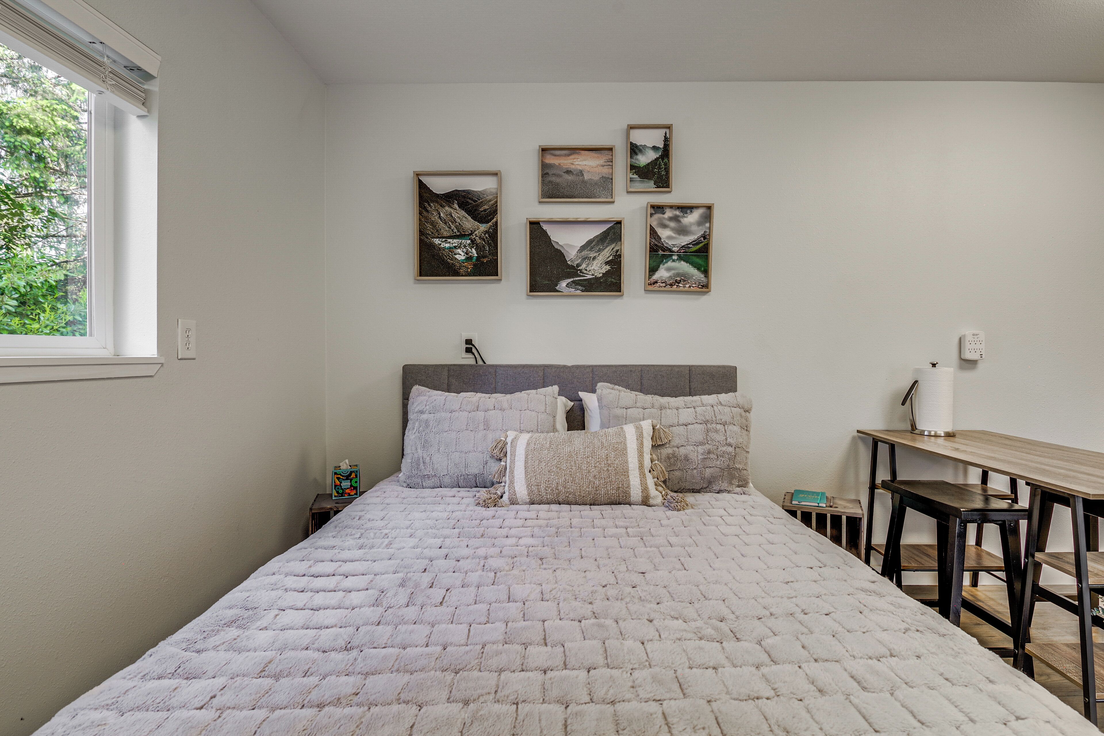 A bedroom with a bed, pillows, a nightstand, a desk, and framed pictures on the wall.