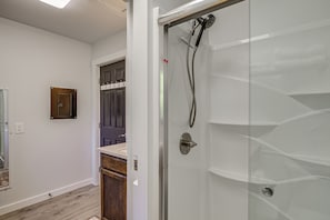 A modern bathroom with a glass shower enclosure, a wooden cabinet, and a countertop. - Pet-friendly Quaint Cottage: Park-like Setting (Monroe)