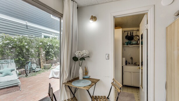 A room with a wooden table and chairs, a white vase with flowers, and a view of the outside. - Cozy Studio w/ Patio & Shared Pool in La Jolla! (La Jolla)