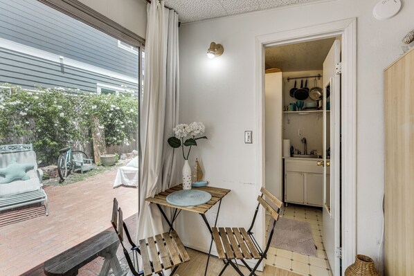 A room with a wooden table and chairs, a white vase with flowers, and a view of the outside. - Cozy Studio w/ Patio & Shared Pool in La Jolla! (La Jolla)
