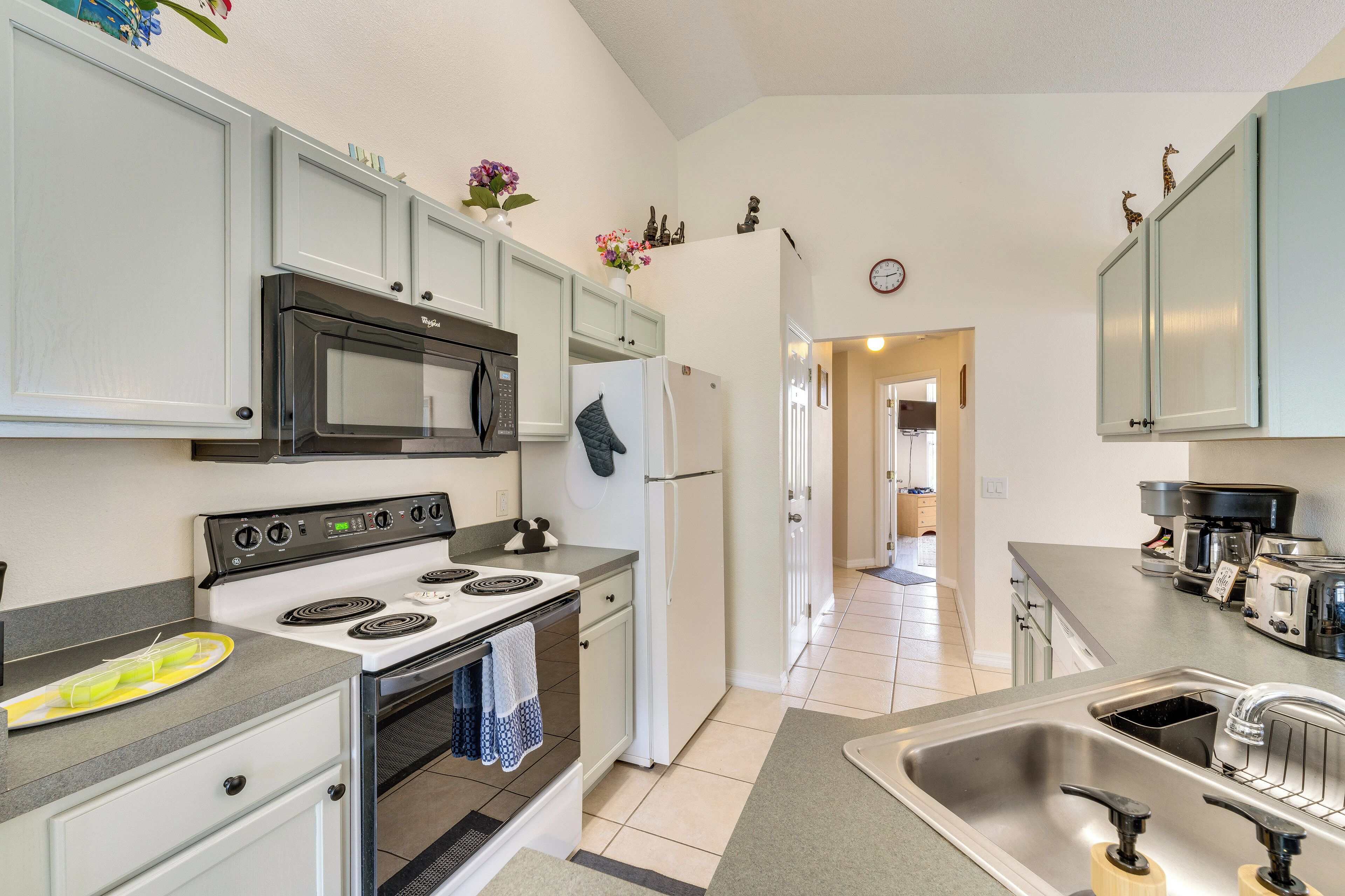 A kitchen with white cabinets, a microwave, stove, refrigerator, and a sink.