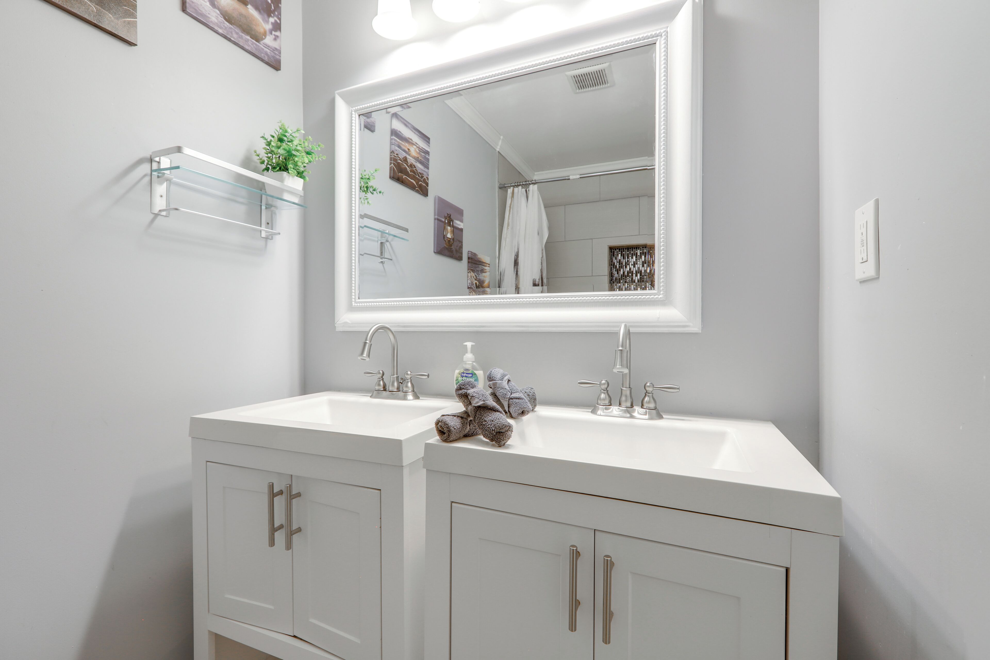A bathroom with a white vanity, a large mirror, two sinks, and a towel rack.