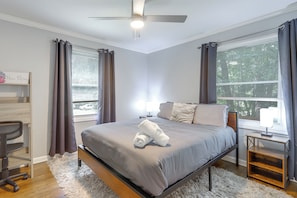 A bedroom with a bed, a desk, a chair, a ceiling fan, and a window with curtains.