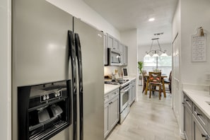 A modern kitchen with stainless steel appliances, a dining area with wooden chairs, and a chandelier. - 3 Mi to Seaworld! Cozy Family Home w/ Patio (San Antonio)