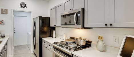 A kitchen with white cabinets, a stainless steel refrigerator, a microwave, a stove, and a sink.