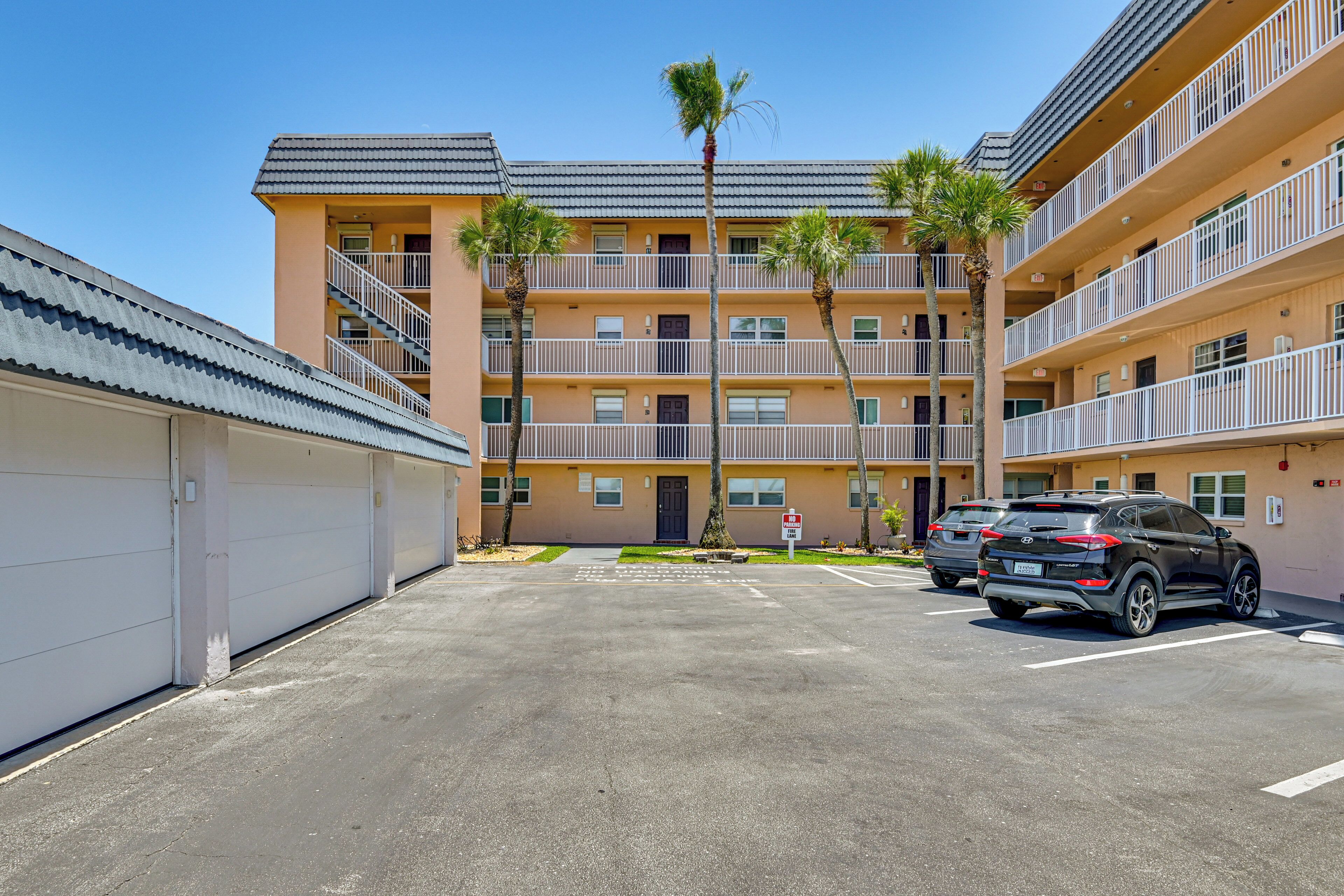A multi-story building with balconies, a parking lot, and two parked cars.