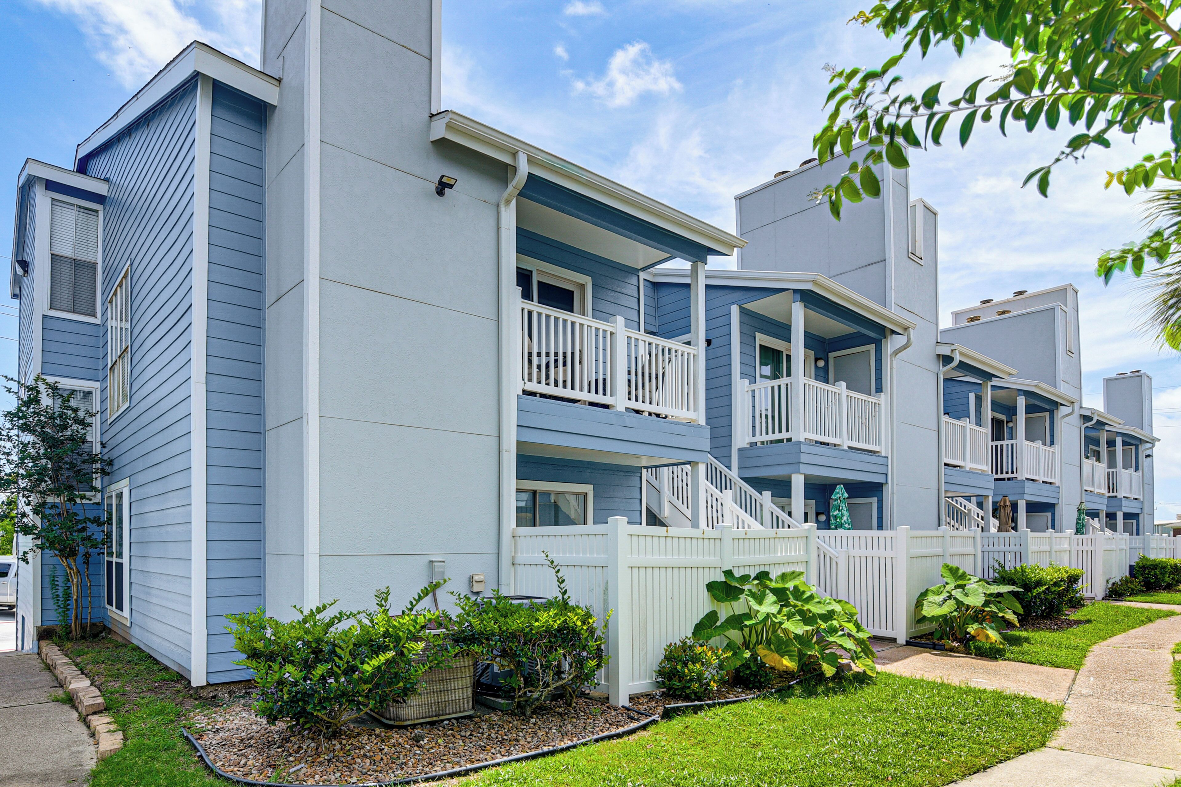 A multi-story residential building with balconies, a white fence, and a well-maintained lawn.