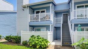 A two-story residential building with a front porch, a staircase, and a small garden area. - Gorgeous Condo Close to Beach and Local Favs (Galveston)