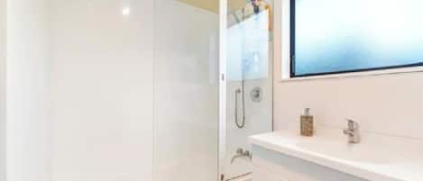 A bathroom with a glass-enclosed shower, a white sink with a mirror, and a wooden floor.