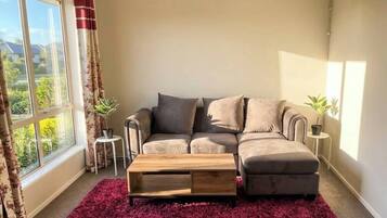A living room with a sectional sofa, a coffee table, a window with curtains, and a small side table with a plant.