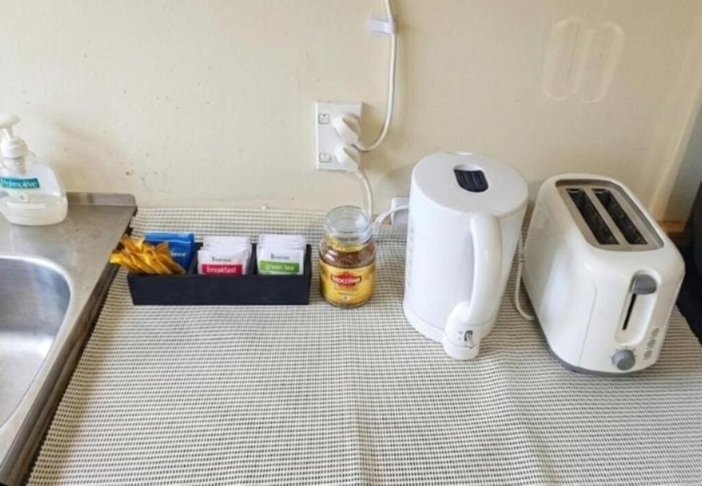 Ett litet kök med en brödrost, en vattenkokare, ett glas med sylt och en flaska handtvål.