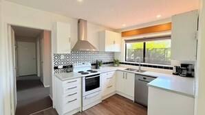 A modern kitchen with white cabinets, a stove, and a sink. - Stylish Tawa Retreat (Wellington)
