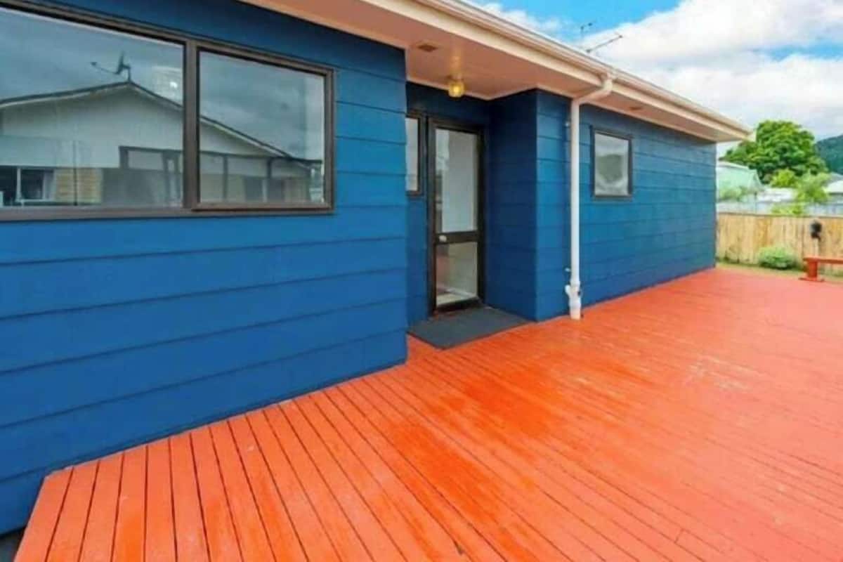 Un edificio azul con una terraza de madera, una puerta y una ventana.