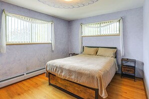 Ein Schlafzimmer mit einem Bett, zwei Nachttischen, einem Fenster mit Jalousien und einer Deckenleuchte.
