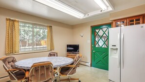 A room with a round table, four chairs, a television, a refrigerator, and a green door. - Extended-stay Home/office, 8 Mi to Dtwn Denver (Lakewood)