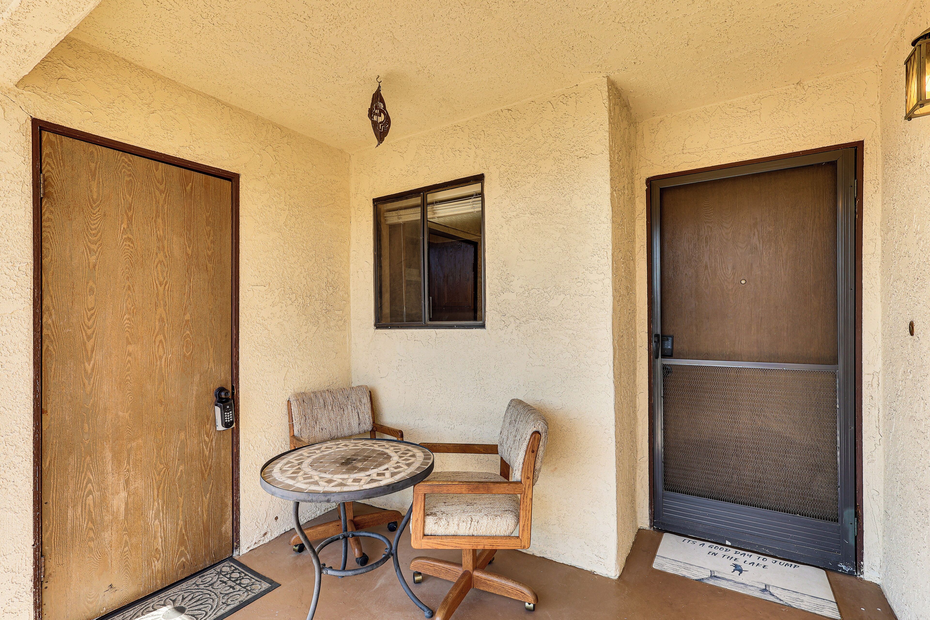 A room with a wooden door, a window, a chair, a table, and a door mat.
