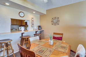 A dining area with a wooden table, chairs, a clock, and a kitchen area with cabinets and appliances. - Poolside Fun, Lake Havasu Views! Desert Getaway (Lake Havasu City)