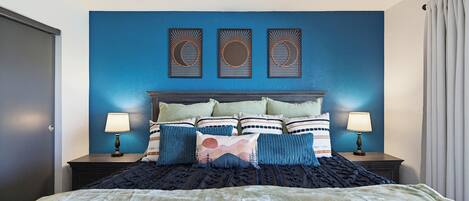 Un dormitorio con una cama, dos mesitas de noche, un cabecero y tres paneles decorativos en la pared.