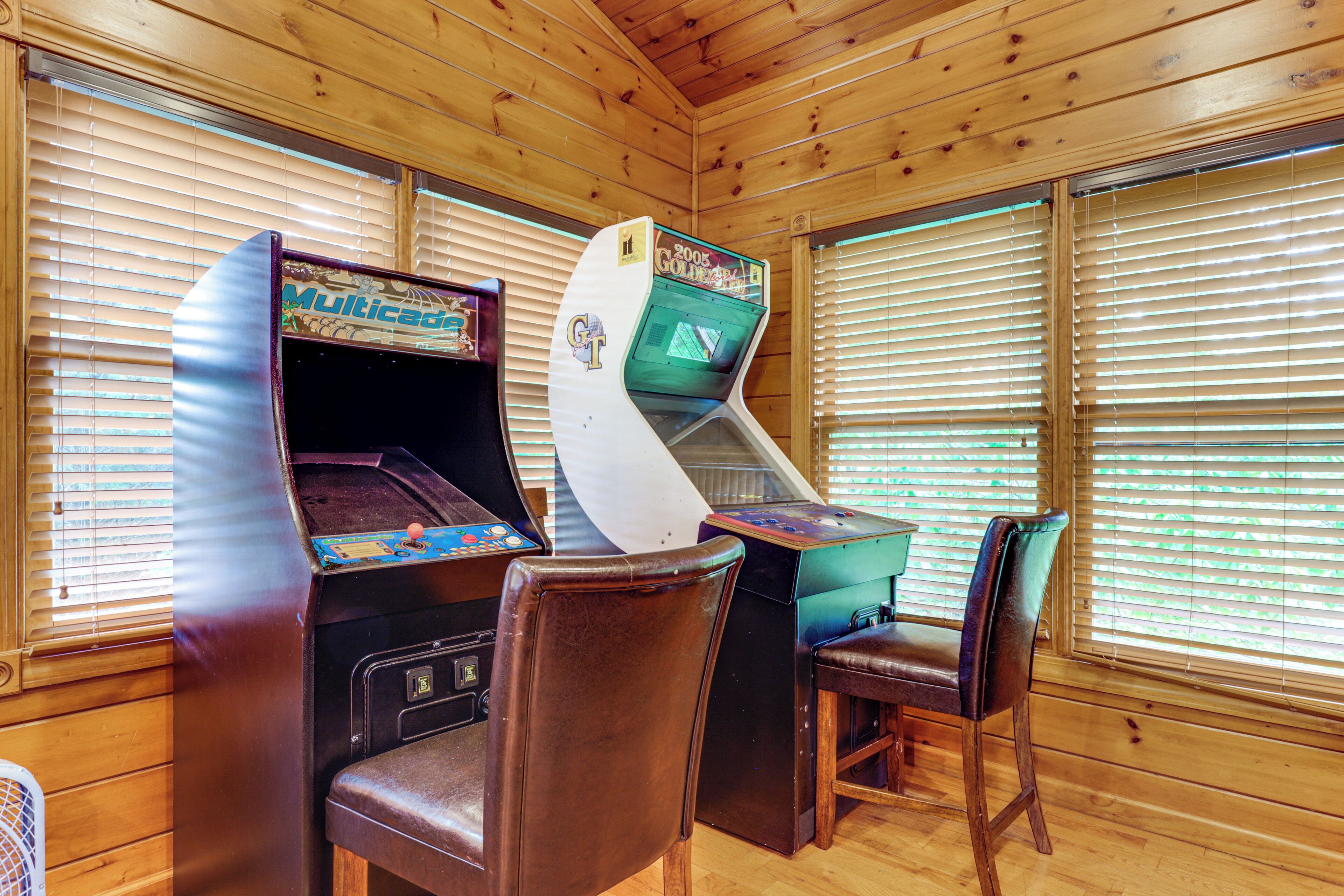 Une pièce aux murs et au plafond en bois, avec deux bornes d’arcade et une paire de chaises.