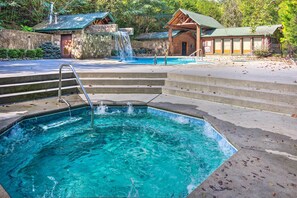 A swimming pool with a waterfall feature, stone steps, and wooden cabins in the background. - Hot Tub & Game Room! Resort Cabin 4 Mi to Gsmnp (Gatlinburg)