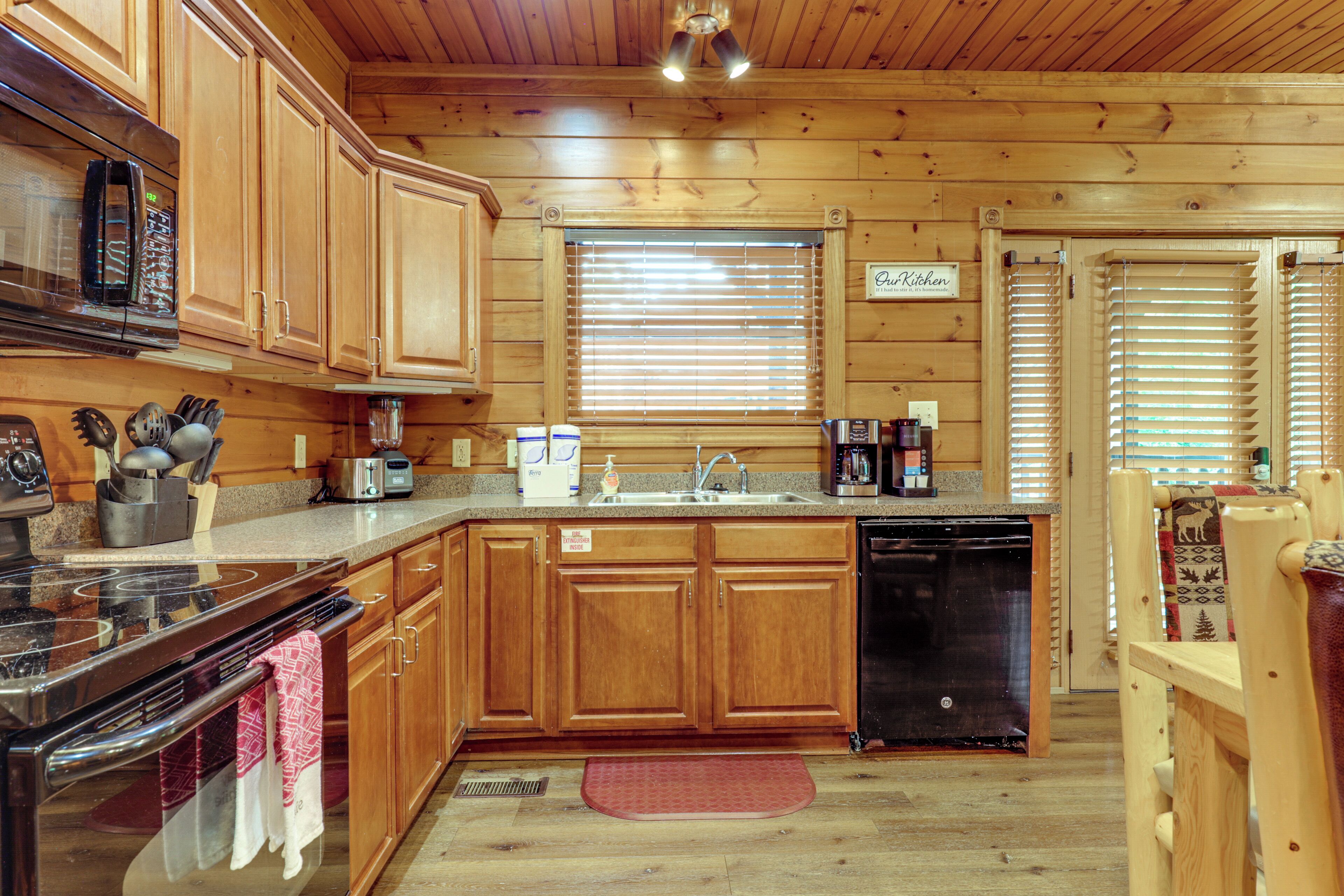 Une cuisine rustique aménagée dans une cabane en bois, équipée d’un four à micro-ondes, d’une cuisinière, d’un évier et d’une pancarte indiquant : « Notre cuisine ».