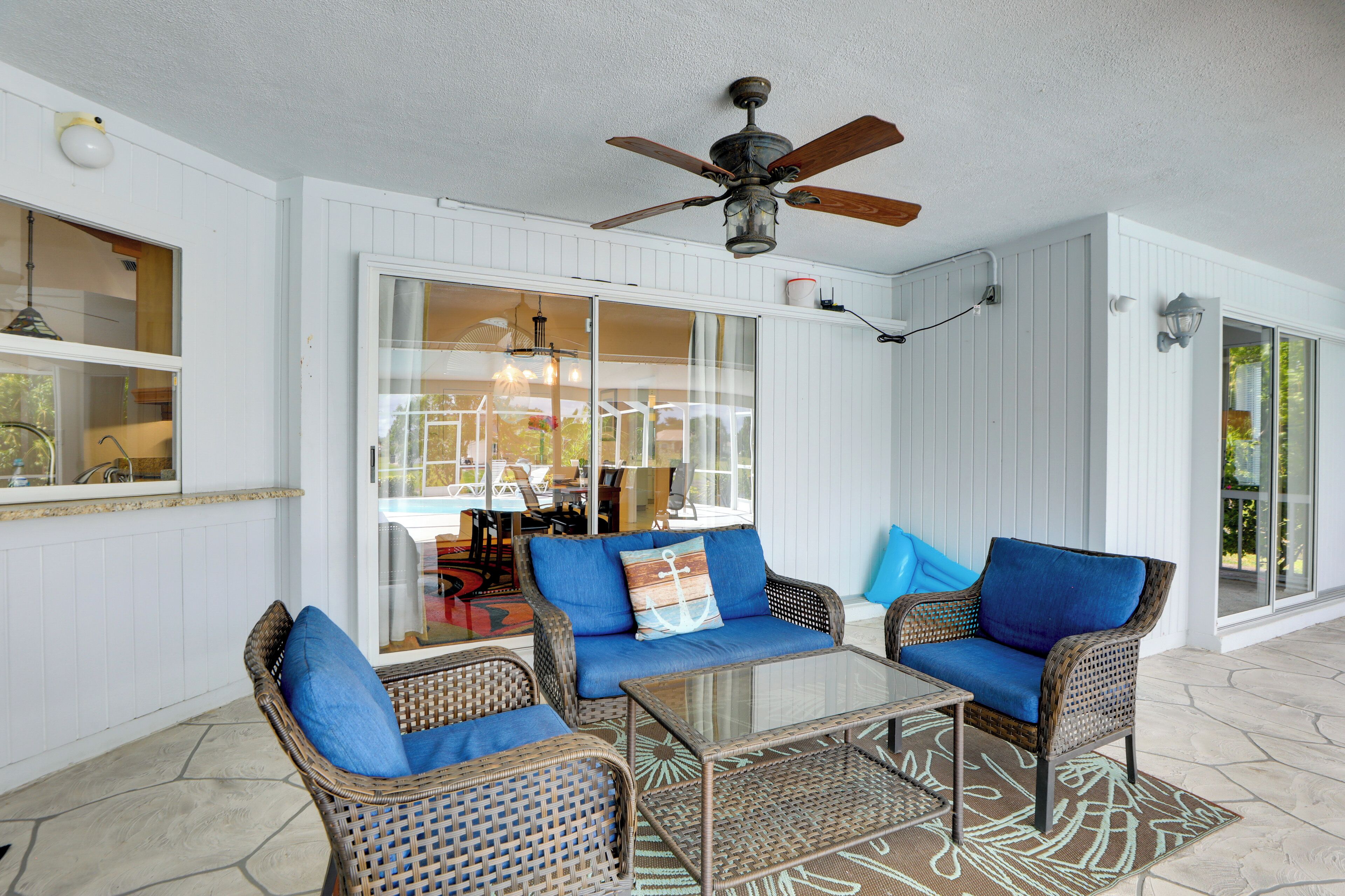A covered patio with wicker furniture, a ceiling fan, and a glass table.