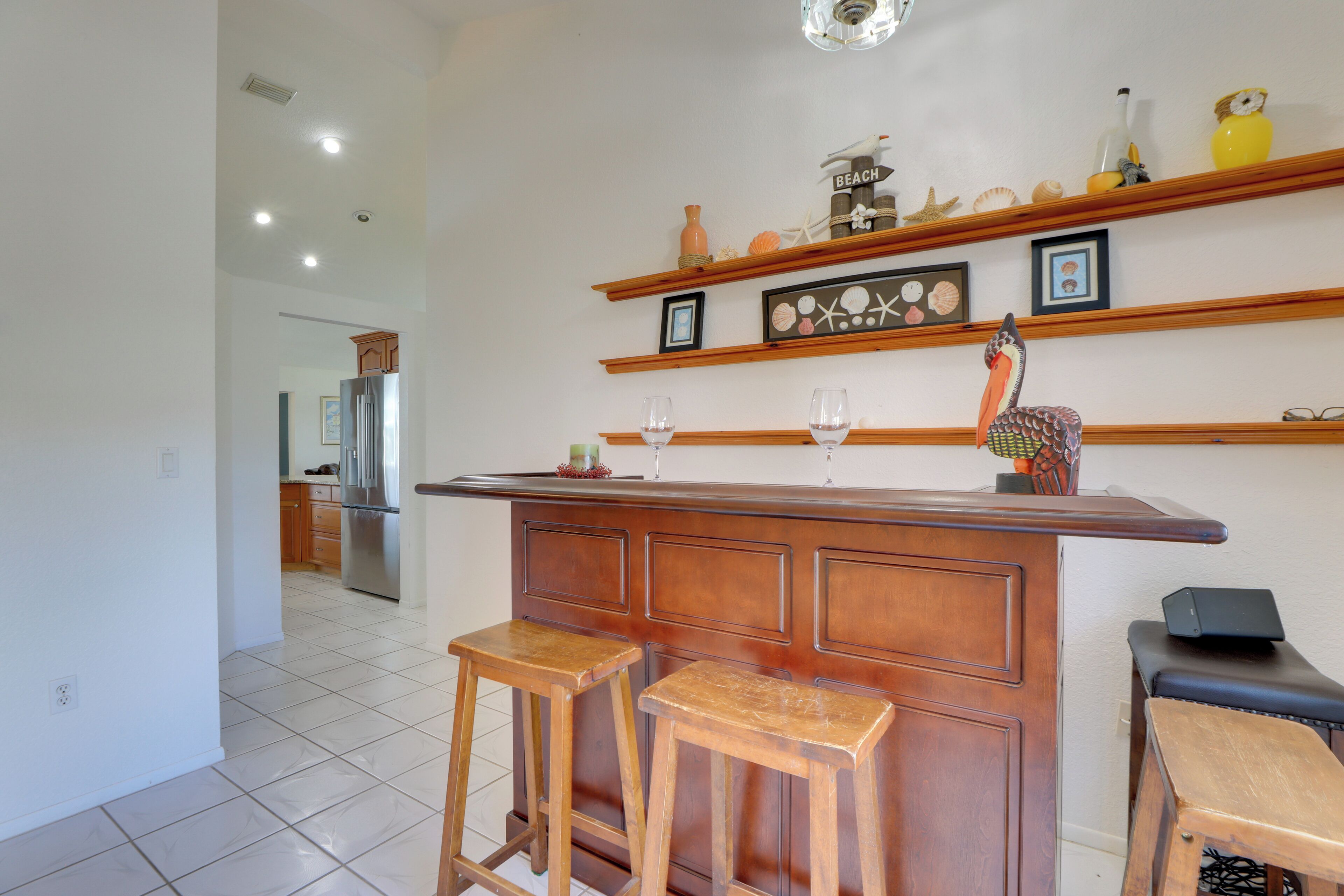 Una cocina con una isla de madera, dos taburetes de bar, un refrigerador y un estante con adornos.
