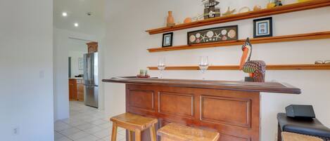 Una cocina con una isla de madera, dos taburetes de bar, un refrigerador y un estante con adornos.