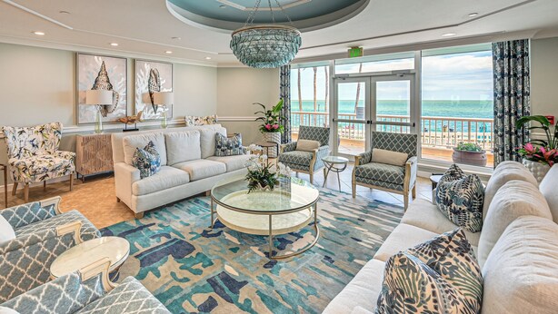 A spacious living room with a large window overlooking the ocean, a round glass coffee table, and a variety of seating options. - Beachfront Condo w/ Wide Balcony in Marco Island! (Marco Island)