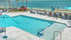 A swimming pool with lounge chairs and umbrellas, a view of the ocean, and a clear sky. - Beachfront Condo w/ Wide Balcony in Marco Island! (Marco Island)