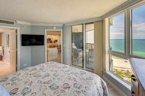 Ein Hotelzimmer mit einem großen Bett, einem Fernseher, einem Balkon mit Blick auf den Strand und einer Schiebetür zum Essbereich.