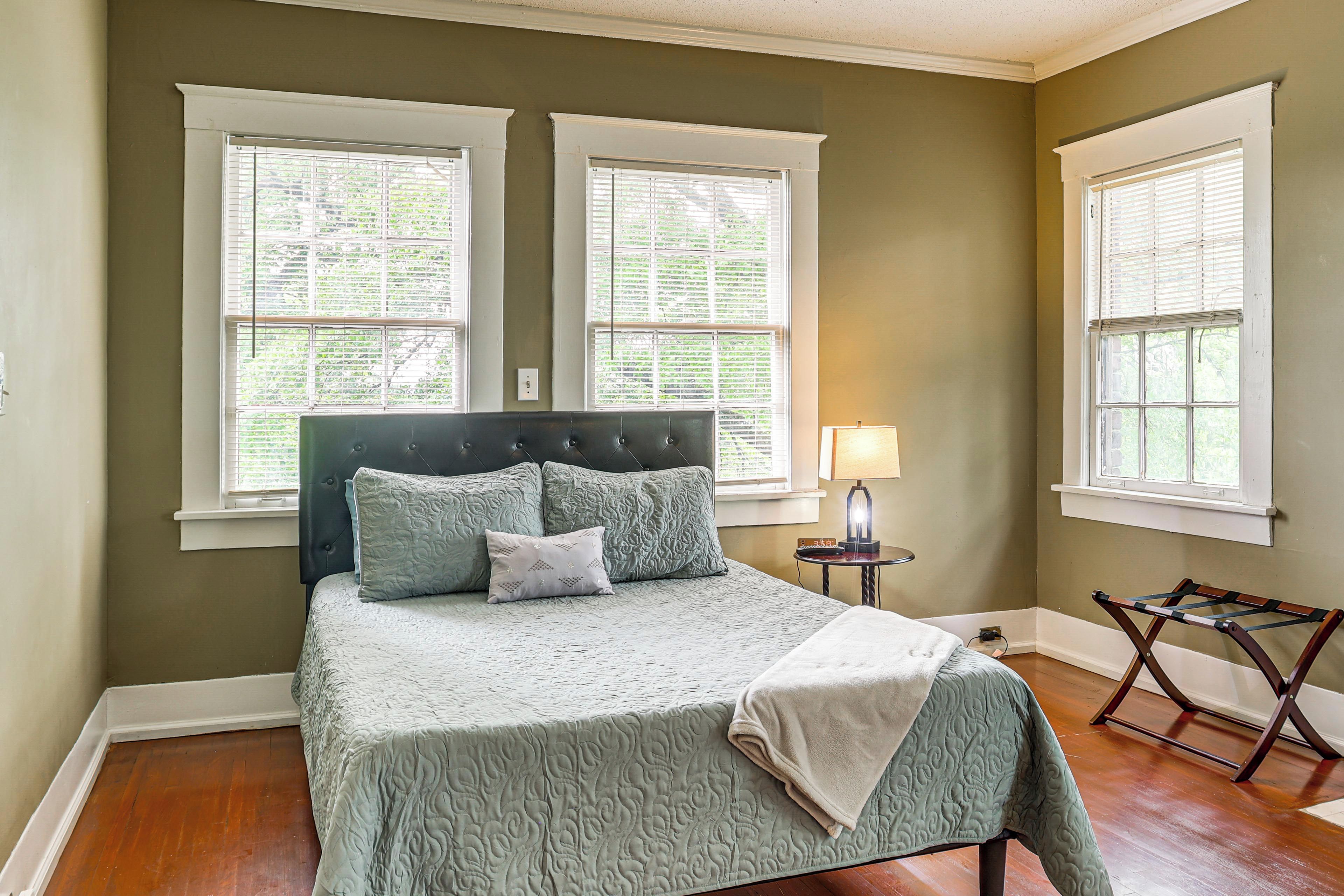 A bedroom with a bed, two windows, a nightstand, and a lamp.
