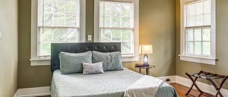 A bedroom with a bed, two windows, a nightstand, and a lamp.