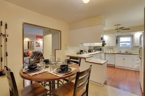 A kitchen with white cabinets, a dining table with chairs, a microwave, and a ceiling fan.