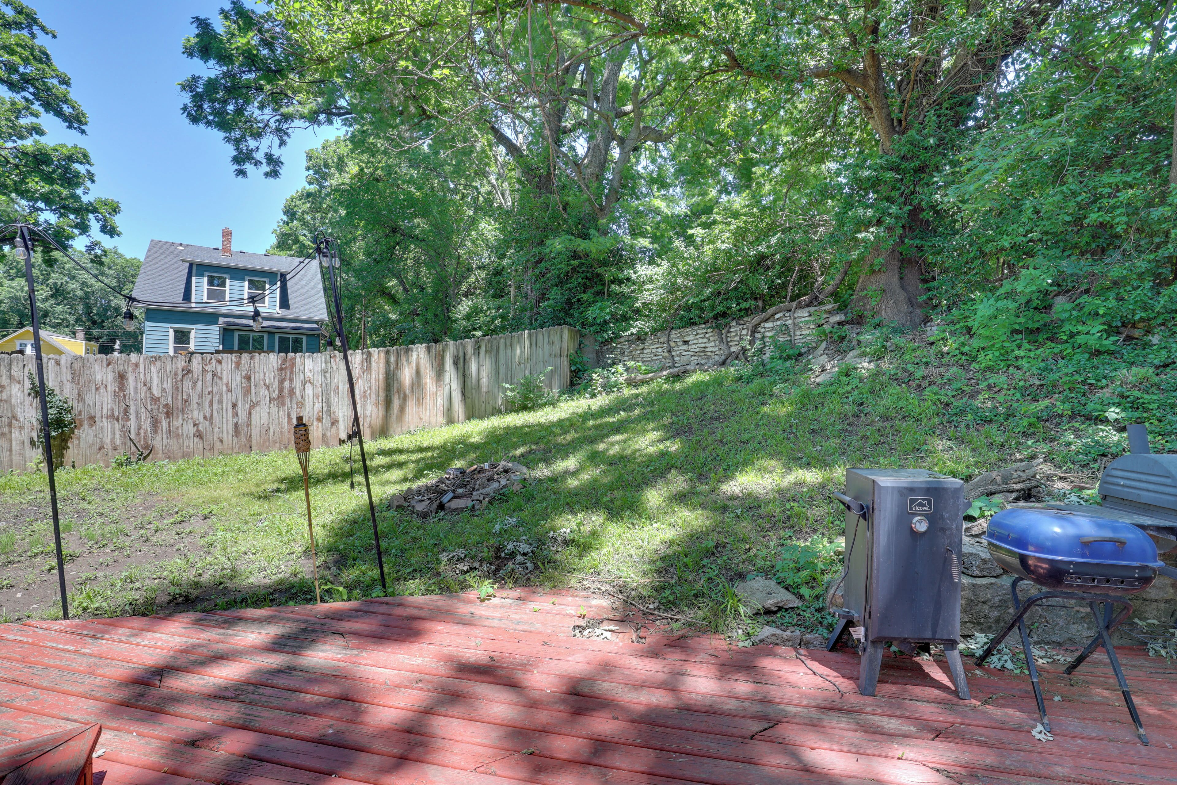 A backyard with a wooden deck, a barbecue grill, and a stone wall.
