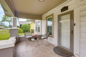 A covered porch with two chairs, a small table with a vase, and a door with a mailbox.