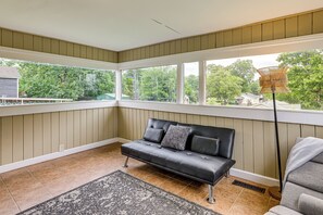 A room with a black leather sofa, a patterned rug, and a view of trees through large windows.