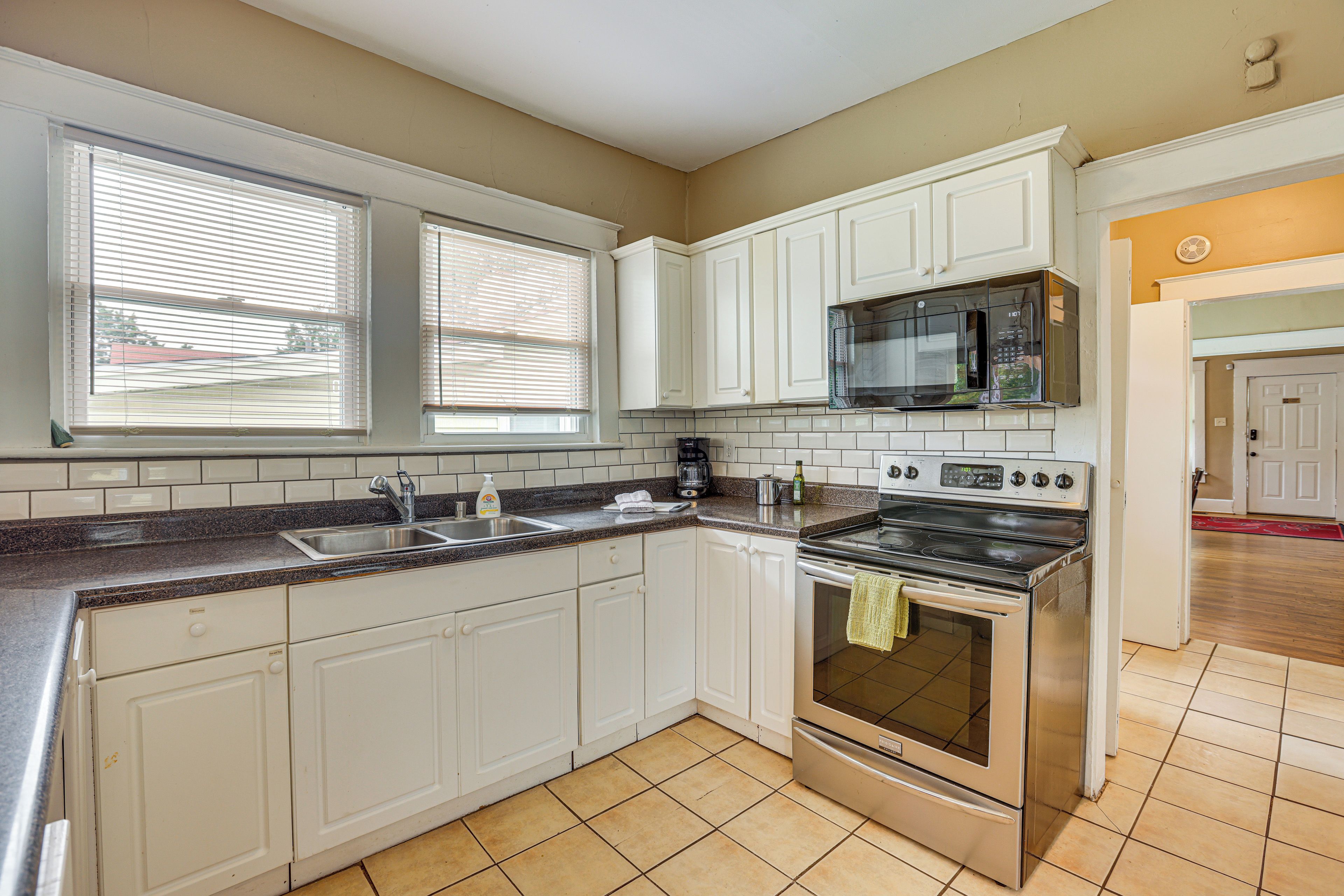 A kitchen with white cabinets, a stainless steel stove, a microwave, and a window with blinds.