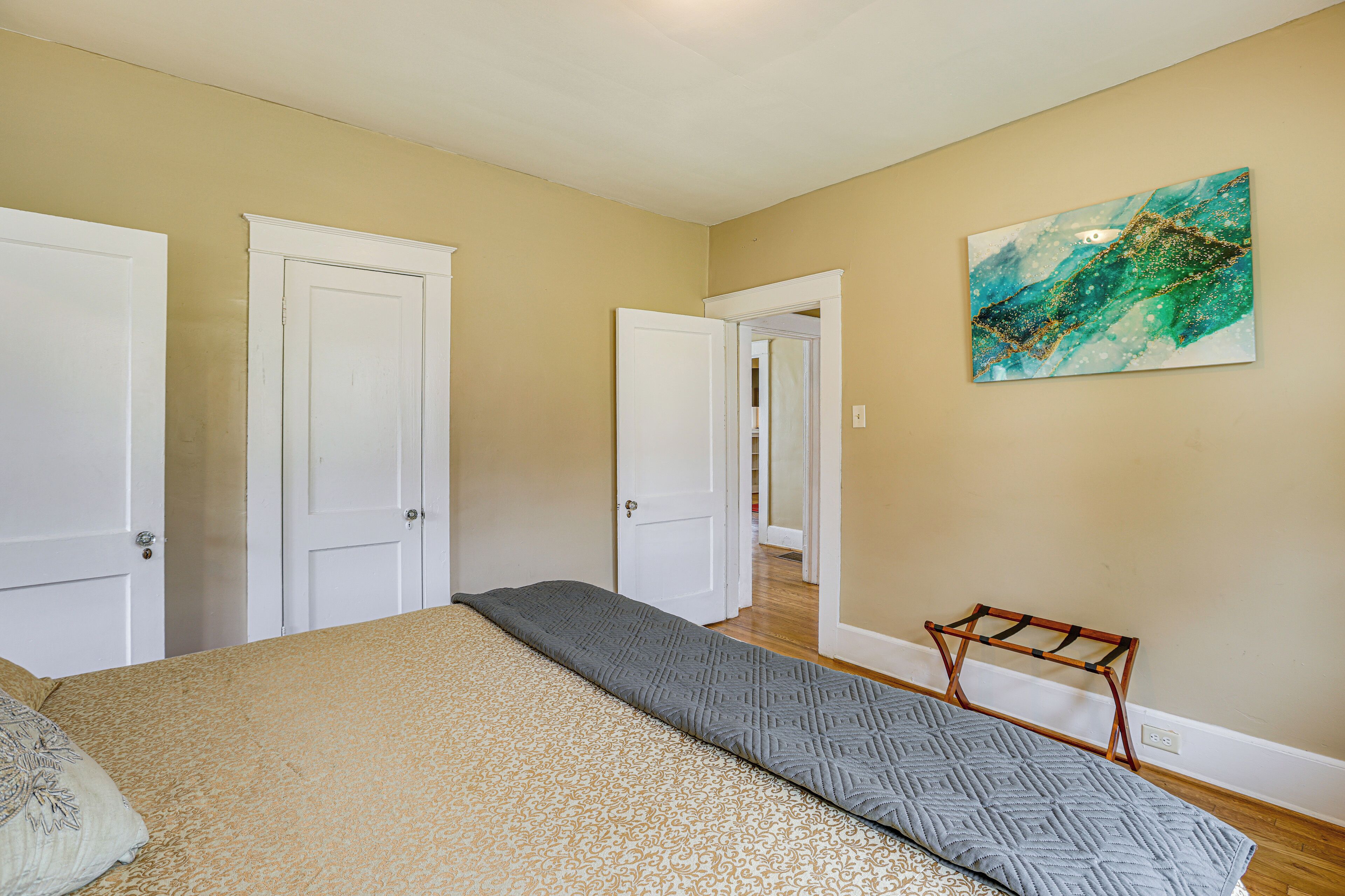 Un dormitorio con cama, una puerta, un pasillo y una obra de arte colgada en la pared.