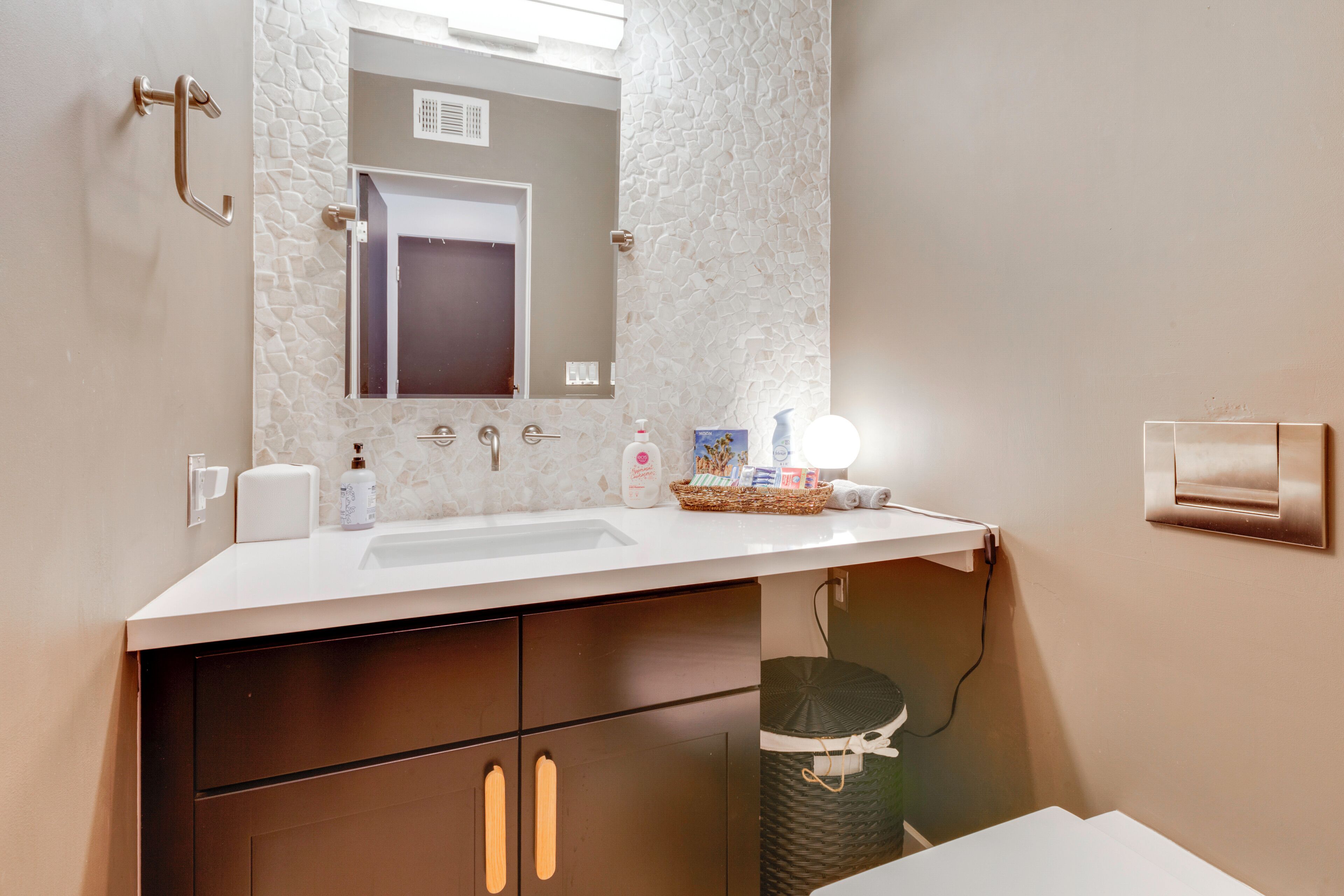 Un bagno con lavandino bianco, specchio, portasciugamani e cestino.