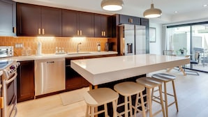A modern kitchen with dark cabinets, stainless steel appliances, a large island with stools, and pendant lighting. - Unwind Poolside, Walk to El Paseo: Desert Oasis! (Palm Desert)