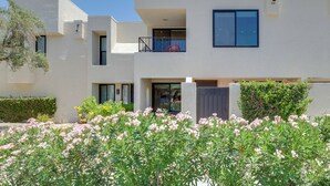 A modern two-story building with a balcony, a gated entrance, and a garden with flowering plants. - Unwind Poolside, Walk to El Paseo: Desert Oasis! (Palm Desert)