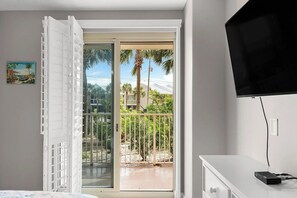 Ein Zimmer mit einer Glastür zu einem Balkon, einem wandmontierten Flachbildfernseher und einem Schreibtisch mit Tastatur und Maus.