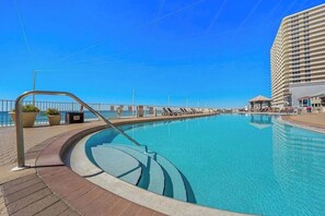 Ein Pool mit gewölbter Kante, einem Metallgeländer und Blick auf ein Hochhaus im Hintergrund.
