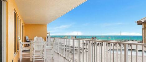 A balcony with a view of the beach, white chairs, and a railing.