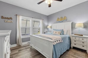 Ein Schlafzimmer mit Bett, Nachttischen, einem Schminktisch, einem Deckenventilator und einem Fenster mit Jalousien.